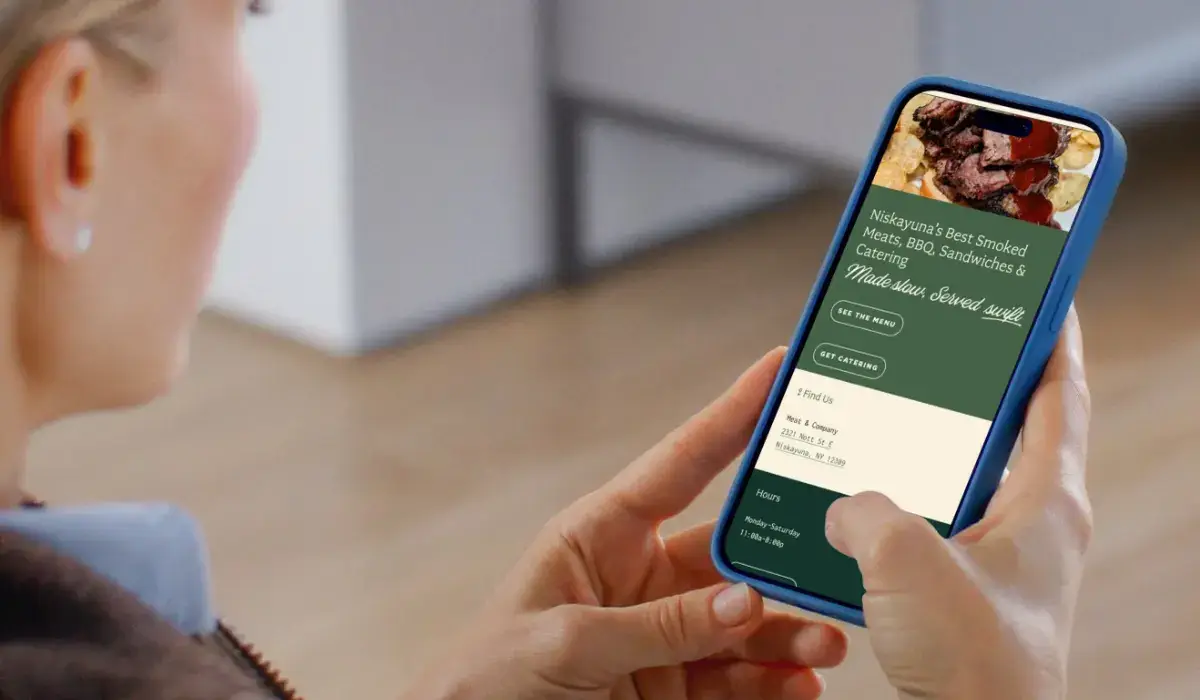 Person browsing the Meat & Company BBQ restaurant website on a smartphone with menu, location, hours, and catering information.